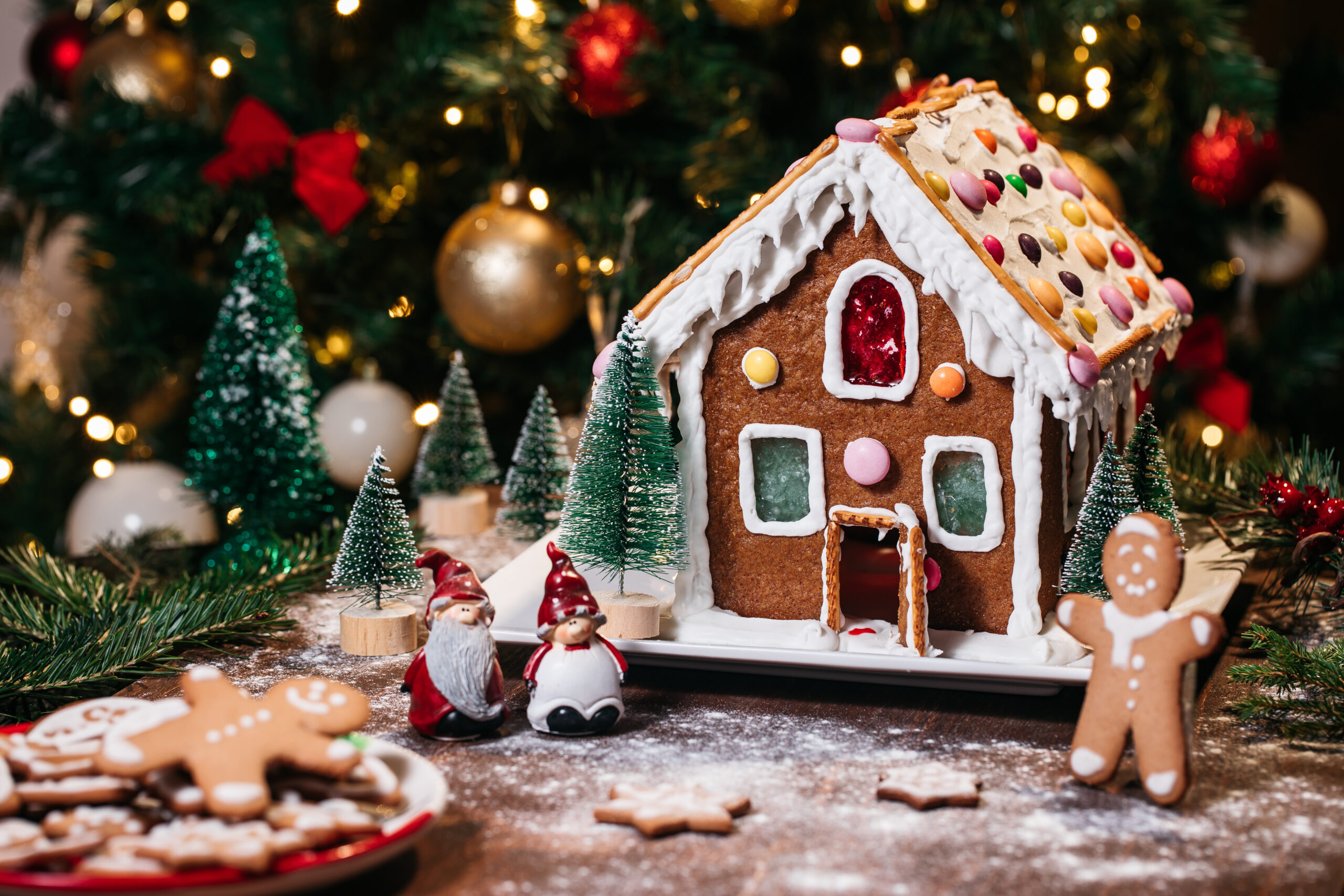 Christmas house from ginger cookies with ginger man outside decorated in Christmas spirit with tree in background