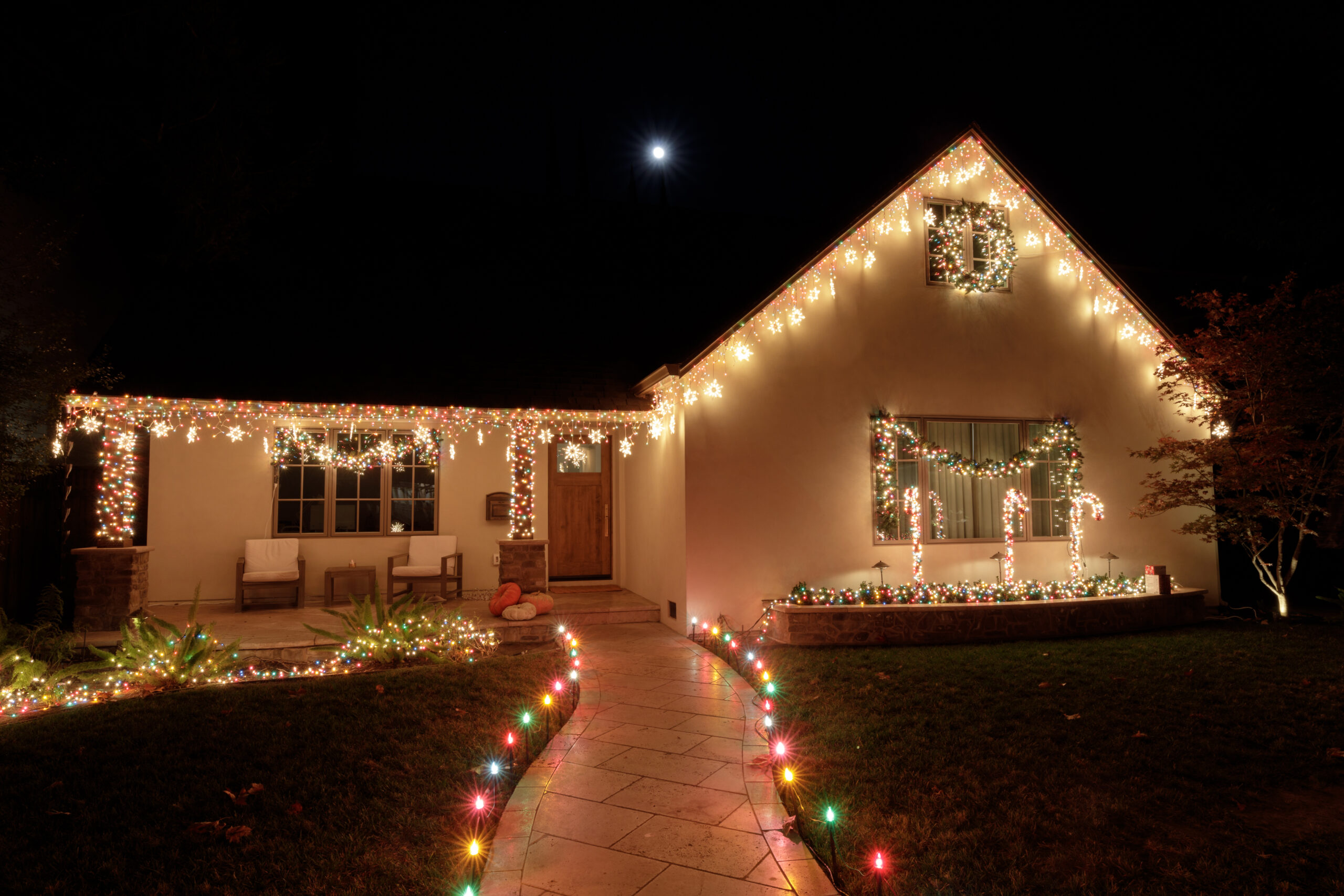 Christmas lights decorating house at night with full moon